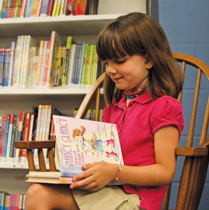 Young girl reading a book inside a library